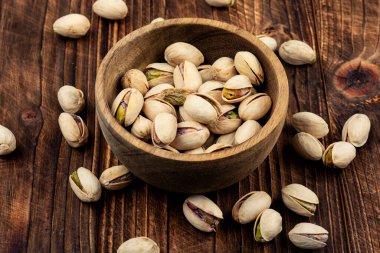 Koyu dokulu yüzeyde sunulan ahşap bir kasede tuzlu şam fıstığı. Sağlıklı vejetaryen protein besleyici gıdalar.