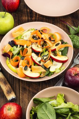 Dilimlenmiş elma, havuç kurdelesi, karışık yeşillik ve tohumdan yapılmış sağlıklı vejetaryen salatası..