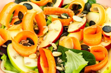 Vitamin elmaları, havuç kurdeleleri, yapraklı yeşillikler ve tohumlarla dolu salata kasesi. Gıda arkaplanı