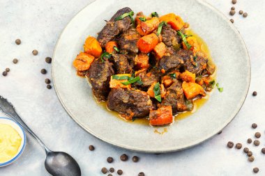 Tatlı patatesle pişirilmiş yumuşak et parçaları ve koyu parlak soslu otlar. Seramik kasede servis edilen konforlu yemekler..