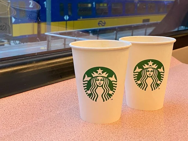 Kawa na dojazdy do pracy w pociągu. Starbucks w pucharze kartonowym. Dworzec kolejowy przez okno. — Zdjęcie stockowe