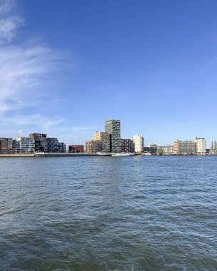 Dordrecht 'ten Zwijndrecht' e uzanan Oude Maas nehrinin karşısındaki panoramik portre manzarasında modern apartman blokları, rıhtım evleri, kentsel yenileme, Hollanda nehir kenarı mimarisi yer alıyor..