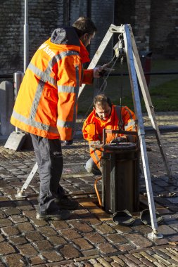 Technical workers repairing automatic bollards set in a cobble paved street clipart