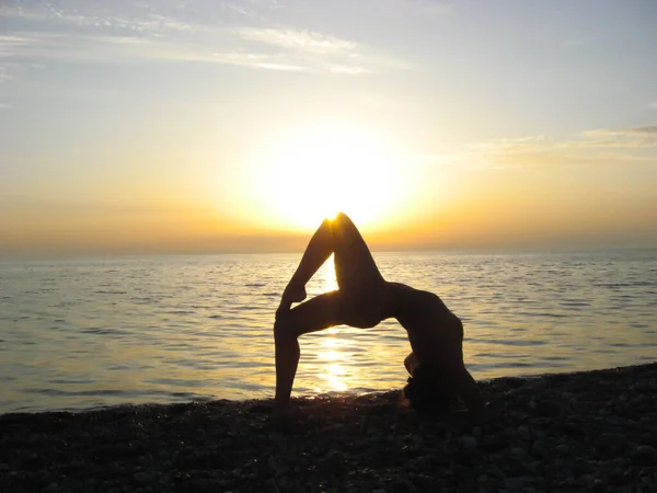 Deniz kenarında yoga yapan kız, gün batımının arka planında siluet, plaj.