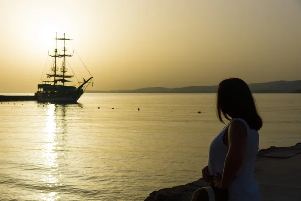 Beautiful sunset over the sea. Sailboat in the bay. Woman standing on the beach and looking at the sea. — Stock Photo, Image