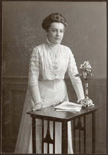 Винтажный портрет молодой женщины, стоящей у стола с журналами и вазой с цветами — стоковое фото