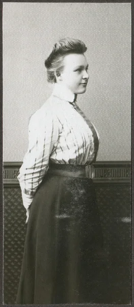 A vintage portrait of young woman, standing half-turned to the wall, dressed in a blouse and long skirt — Stock Photo, Image