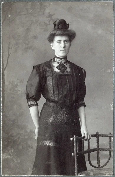 Portrait vintage d'une femme, debout près de sa chaise, vêtue d'un chemisier noir et d'une longue jupe noire — Photo