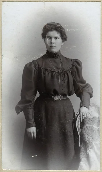 A vintage portrait of a woman, standing near the chair and dressed in a dress — Stock Photo, Image