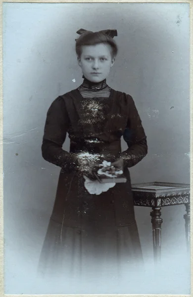 Un portrait vintage d'une jeune femme, debout près d'une table et tenant un livre dans ses mains — Photo