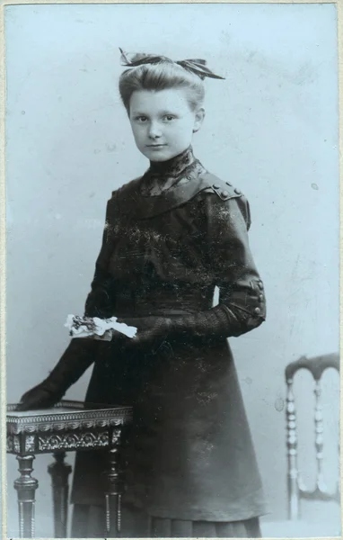 Un portrait vintage d'une jeune femme, debout près d'une table et tenant un livre dans ses mains — Photo