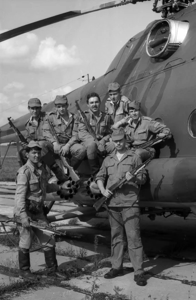 A squad of soldiers standing near a combat helicopter Mi-8. Film scan. Large grain — Stock Photo, Image