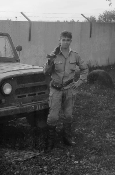 A soldier with a gun standing near army SUV UAZ-469. Film scan. Large grain — Stock Photo, Image