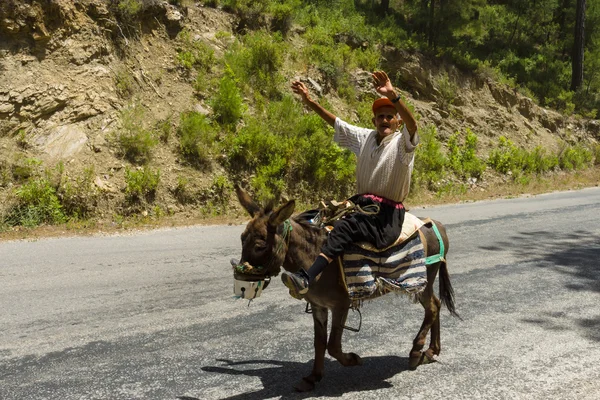 Village resident entertains tourists riding on a donkey — Stock Photo, Image