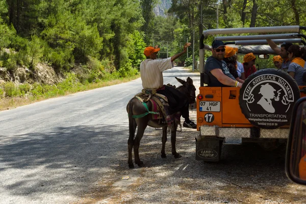 Village resident entertains tourists riding on a donkey — Stock Photo, Image