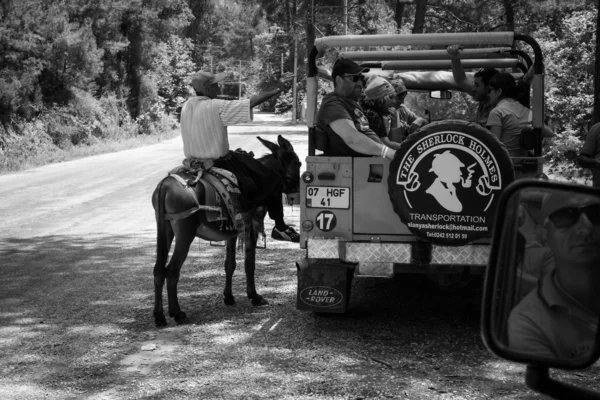 Village resident entertains tourists riding on a donkey. Black and white — Stock Photo, Image