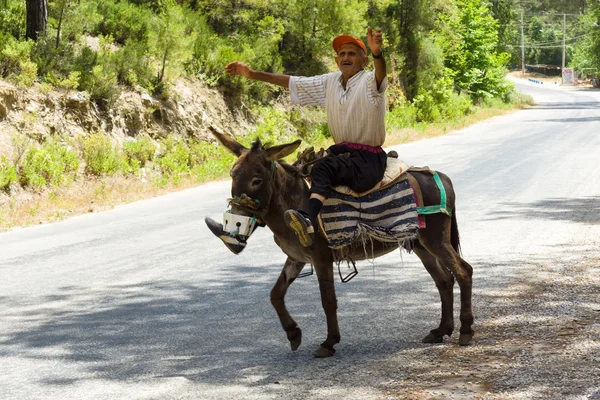 Village resident entertains tourists riding on a donkey — Stock Photo, Image