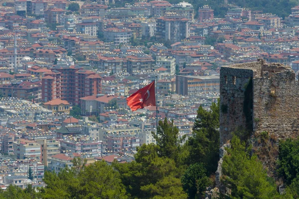 Den turkiska flaggan på bakgrund av husen i det centrala distriktet Alanya. Visa från den gamla fästningen i Alanya. — Stockfoto