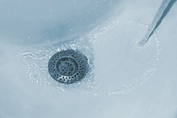 Agua que fluye por el agujero en un fregadero de cocina . —  Fotos de Stock