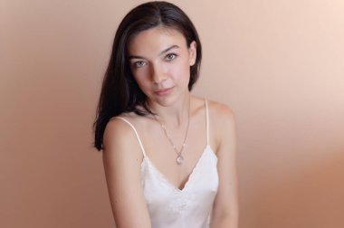 Bej duvar arkasında poz veren güzel genç bir kadın..