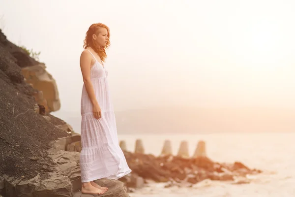 Rödhårig kvinna som står vid kusten på stranden. — Stockfoto