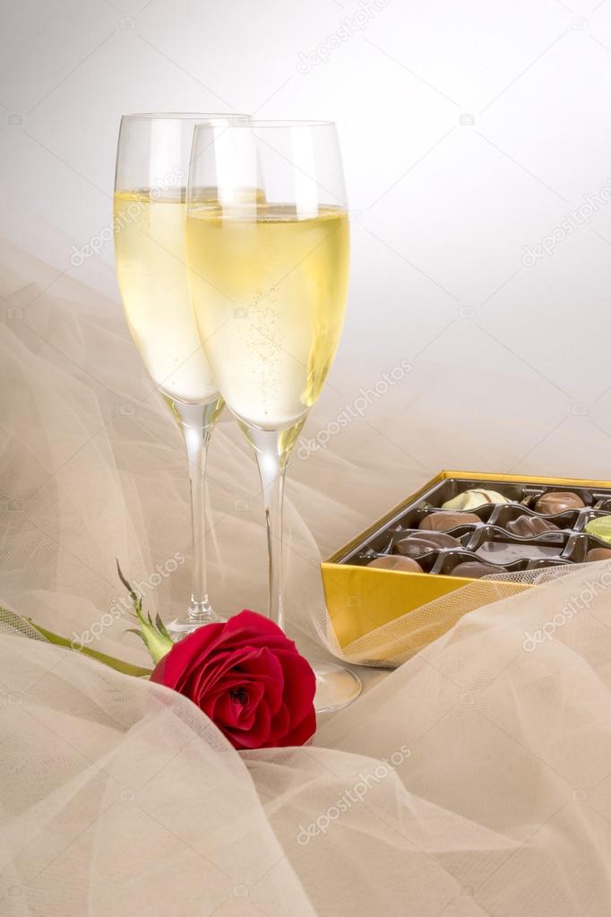 Two Glasses of Champagne, Single Red Rose and an Open Box of Gourmet Chocolates