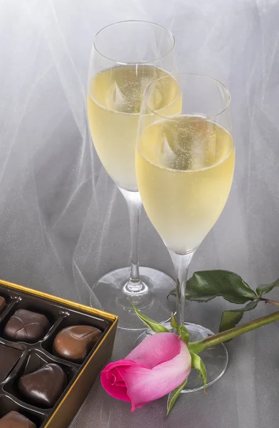 Deux verres de champagne, une rose simple et une boîte ouverte de chocolats gourmands — Photo