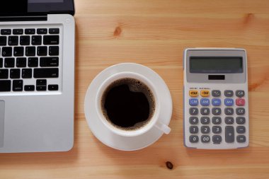 Dizüstü bilgisayar, hesap makinesi ve beyaz bardakta sade kahve fotokopi masası, üst manzara. Muhasebeci, Hesaplama, Vergi İdaresi.