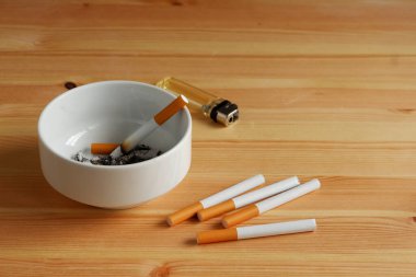 Beyaz küllüğü ve çakmağı olan bir sürü sigara, yazı için kopyalama alanı olan ahşap masa. Stres atmak için sigara içmek ama sağlıksız..