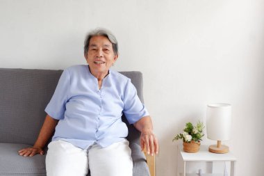 Kanepede mutlu bir şekilde gülen yaşlı Asyalı kadın, yaşlanan toplum, yaşam kalitesi ve sağlık konsepti, metin için fotokopi alanı.