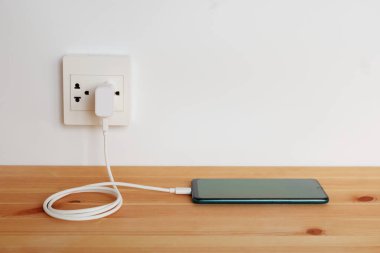 Elektrik prizine bağlı ahşap zemindeki akıllı telefonun şarj kablosu.