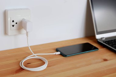 Elektrik prizine bağlı ahşap zemindeki akıllı telefonun şarj kablosu.