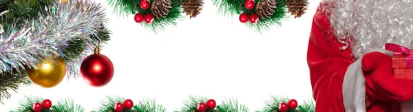 サンタクロースが赤いギフトボックスを持っているのを撮影 装飾されたクリスマスツリーの枝と赤い果実 コーンと松の小枝に囲まれた真ん中のスペースをコピーします バナーサイズ 白地に隔離された — ストック写真