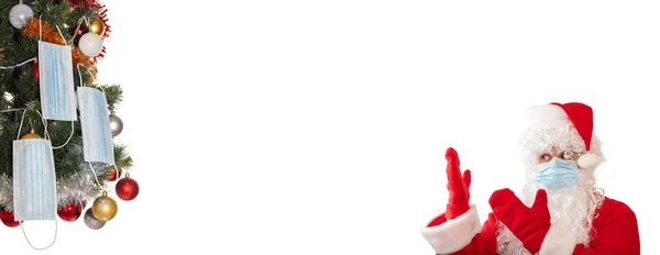 Санта Клаус Медицинской Маске Указывает Обеими Руками Елку Украшенную Шарами — стоковое фото