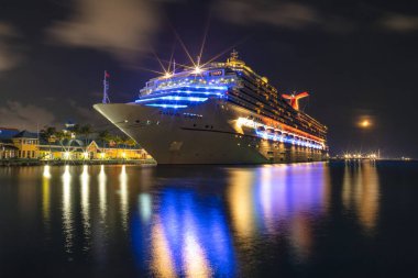 Nassau, Bahamas - June 8, 2019: Beautiful Carnival Liberty cruise ship docked in Prince George Wharf at night. Gorgeous reflections of the ship's, port's lights in the harbour water in the foreground.