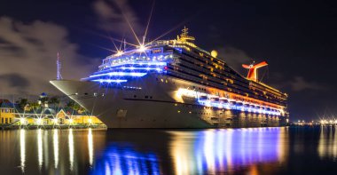 Nassau, Bahamas - June 8, 2019: Beautiful Carnival Liberty cruise ship docked in Prince George Wharf at night. Gorgeous reflections of the ship's, port's lights in the harbour water in the foreground.