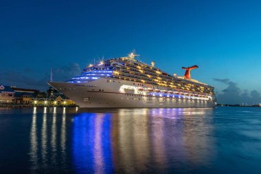 Nassau, Bahamas - July 13, 2019: Carnival Liberty cruise ship docked in Prince George Wharf. Blue hour. Gorgeous reflections of the ship's and port's lights in the harbour water in the foreground. clipart