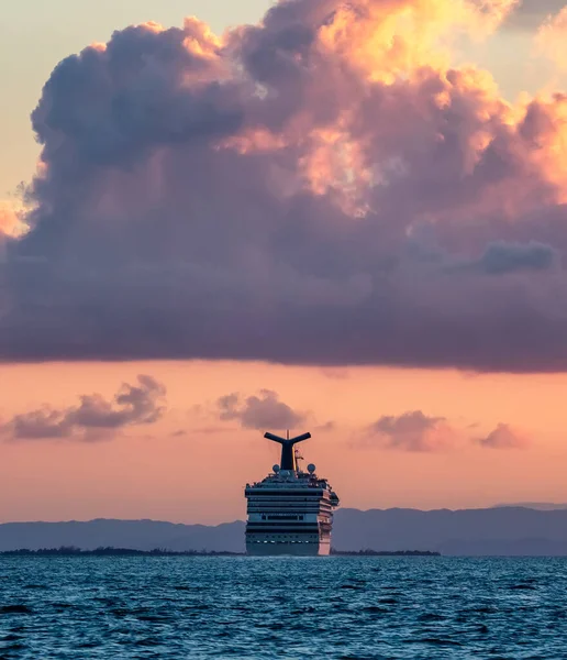 伯利兹海岸 2020年1月1日 日落时在伯利兹海岸航行的嘉年华征服 蓝色海水在前景中 背景是美丽的乌云橙色的天空 免版税图库图片