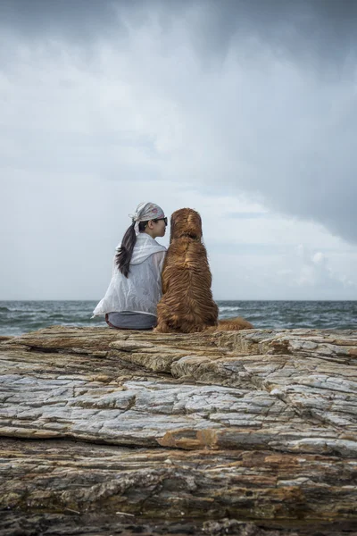 Κορίτσια και Γκόλντεν Ριτρίβερ που κάθεται πάνω στα βράχια της παραλίας — Φωτογραφία Αρχείου
