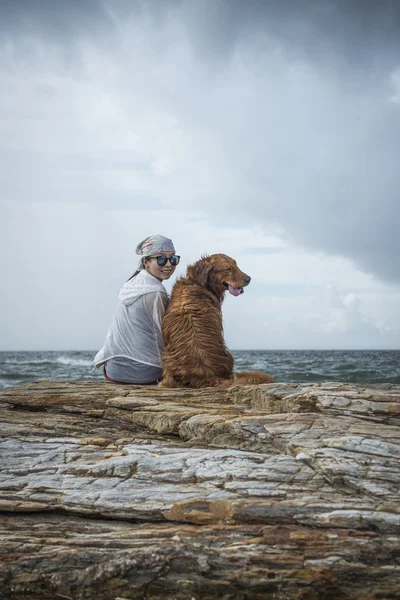 Dziewczyny i złoty pies myśliwski siedząc na skały plaża — Zdjęcie stockowe