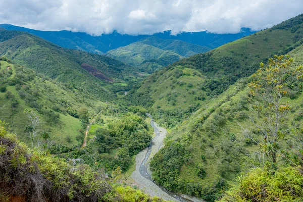 Bulutlu bir gökyüzünün altında dolambaçlı bir nehrin yer aldığı yeşil dağlar ve vadiler.