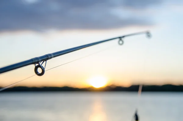 Fishing rod with lure at sunset over a lake — Stock Photo, Image