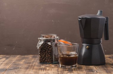 Kahve çekirdekleri ve kahve makinesi ile bir bardak kahve. Seçici odaklanma. Bardakta sade kahve ve kahverengi arka planda kahve makinesi olan cam kavanozda tahıllar..