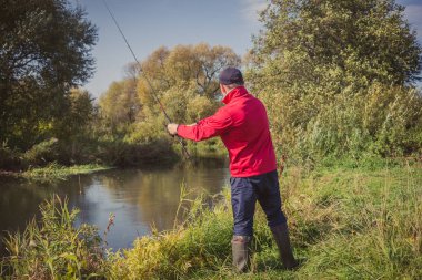 Nehir kıyısındaki adam bir döner çubuk fırlatır. Spor balıkçılığı. Güneşli bir günde balık tutmak