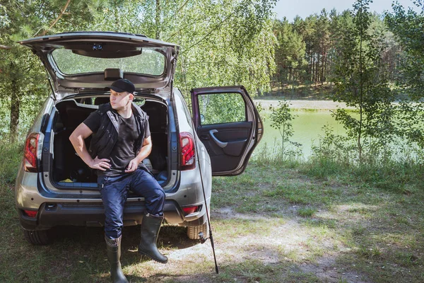 Fishing near the car in nature. Rest at nature. Man prepares fishing tackle near the car in nature