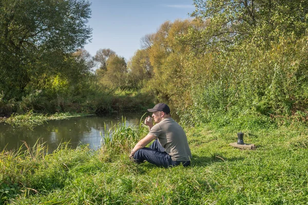 マグカップを持った若い男が自然に座っている — ストック写真