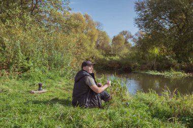 Elinde kupa olan genç bir adam doğada oturuyor. Turizm.