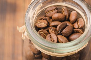 Ahşap bir masada cam bir kavanozda kahve. Üst Manzara. Tahta bir masada açık cam bir kavanozda kahve taneleri..