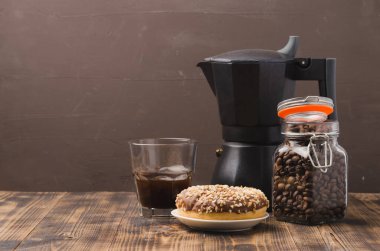 Kahve çekirdekli kahve fincanı ve kahve makinesi. Seçici odaklanma. Bir fincanda sade kahve, fındıklı çörek ve kahverengi arka planda kahve makinesi olan bir kavanozda tahıl..