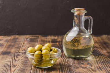 Ahşap masada zeytin yağı şişesi ve zeytin. Seçici odaklanma. Şişedeki zeytinyağı ve arka plandaki koyu renkli fiyonk içindeki zeytin meyveleri ve fotokopi alanı